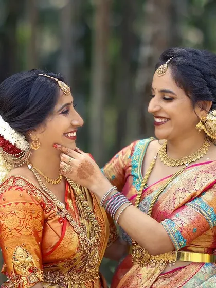 A heartwarming portrait of two sisters, both dressed in beautiful traditional sarees, sharing a happy moment on the wedding day.