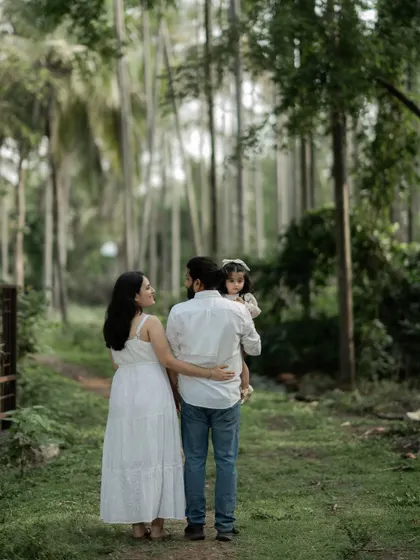 A family of three walks away down a path lined with tall trees. The father holds their daughter, and the mother's arm is wrapped around him, a simple portrait of their journey together. One day, these photos will mean everything.