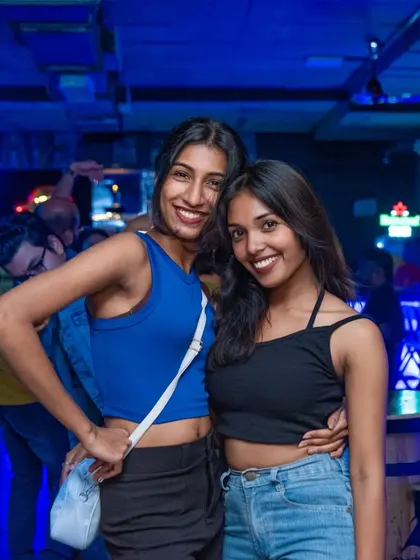Two friends posing for a stylish photo on the dance floor. The blue lighting and neon signs create a perfect club atmosphere.