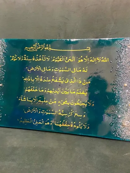 An Ayat al-Kursi piece with an emerald green background and textured borders of silver and gold pearls and crystals.