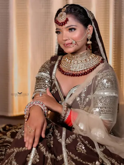 A graceful seated portrait. The bride's pose is elegant and poised, highlighting the beautiful fall of her shimmery dupatta and the heavy embroidery of the lehenga.