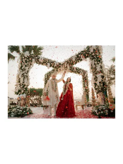A wide-angle shot of the Varmala ceremony, showing the grand floral arch and the shower of petals against the sky.