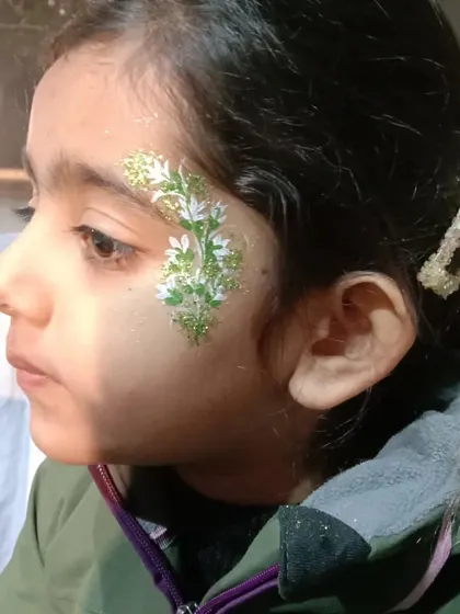 A leafy green and white design with glitter, creating a beautiful botanical pattern on a child's face.