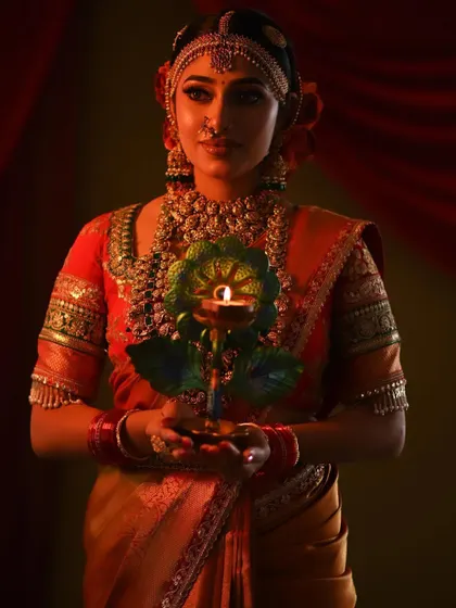 This festive look, perfect for Diwali or a wedding ritual, features a stunning red and orange saree. The warm lighting highlights the rich silk and gold jewelry.