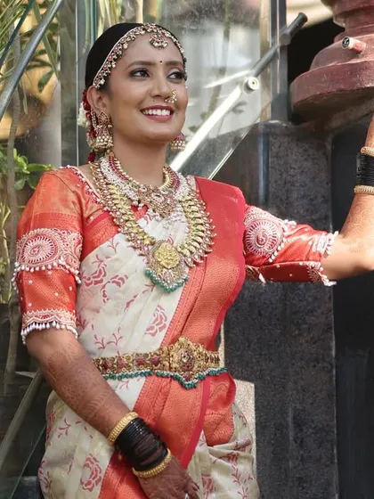 A happy client looking radiant on her wedding day. She chose a beautiful kemp and pearl jewellery set that perfectly matches her off-white and orange saree.