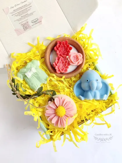 A curated gift box for a baby shower, featuring a clay pot candle, baby elephant candle, onesie sachet, and daisy sachet.
