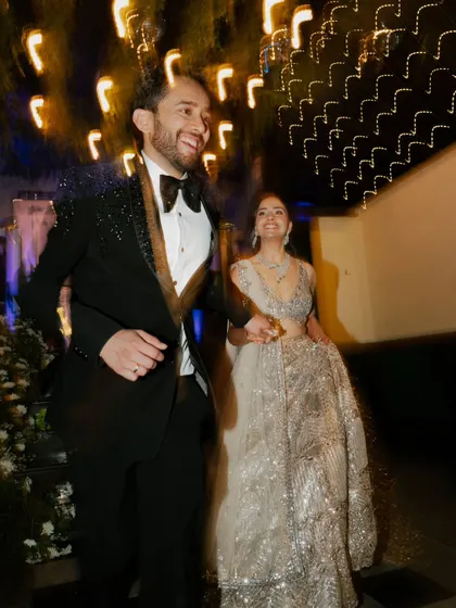A candid, motion-filled shot of the couple making their entrance. The blur of lights and movement captures the exhilarating rush of the Sangeet night.
