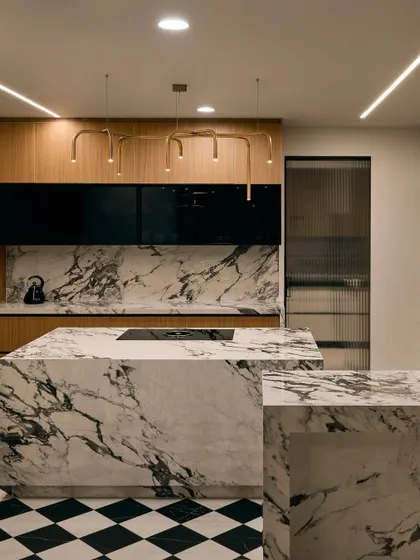 For this Bangalore kitchen, we went for a bold and classic look. A striking black and white marble island is the centerpiece, complemented by black and white checkered flooring. To add warmth, we used wood veneer cabinets and finished the space with modern gold pipe-style lights.