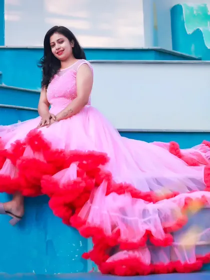 A stylish maternity photo of a woman in a pink and red ruffled trail gown, sitting on a blue staircase.