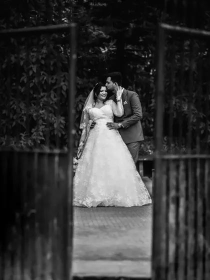 A classic black and white wedding portrait, framed by an open gate. This composition creates a sense of invitation into the couple's story.
