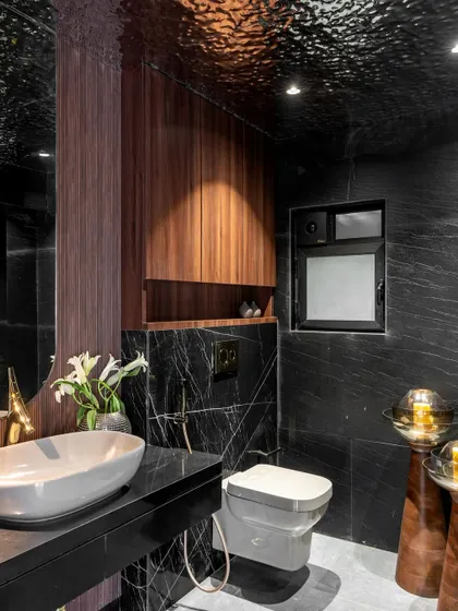 This powder room uses dark, moody tones to create a dramatic effect. The textured ceiling, black marble walls, and warm wood cabinetry combine to form a space that is both intimate and luxurious.