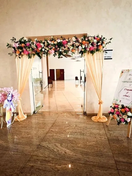A welcoming entrance for a naming ceremony, featuring a floral arch over the doorway, peach drapes, and a custom welcome sign.
