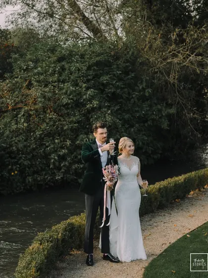 The bride and groom share a champagne toast by the river, celebrating their union in the idyllic landscape of the Cotswolds.