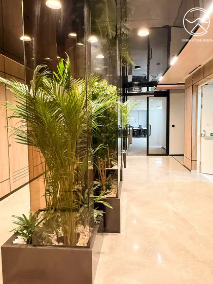 A hallway at The Executive Centre, Hyderabad, where planters are used to soften the hard lines of the architecture. The reflection in the glass walls amplifies the green elements, creating a sense of a larger, more immersive natural environment.