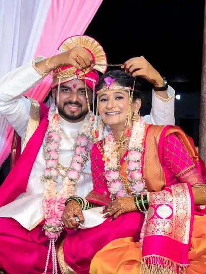 A joyful moment as the groom helps the bride with her headpiece, both of them smiling brightly.
