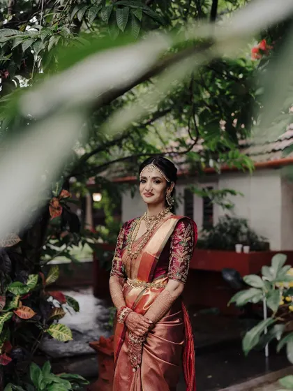 This portrait captures the bride's elegance amidst a natural, rustic setting. The soft focus of the foreground foliage draws the viewer's attention to her serene expression and beautiful attire.