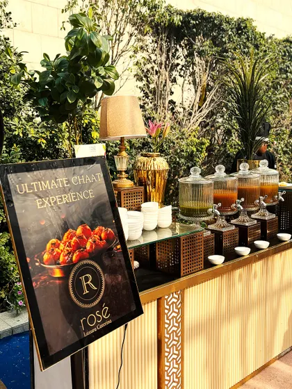 An outdoor setup for our "Ultimate Chaat Experience." The natural greenery provides a beautiful backdrop for our stylish counter and branded signage.