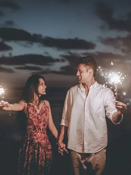 A romantic shot of the couple holding sparklers and looking at each other, with the night sky behind them.