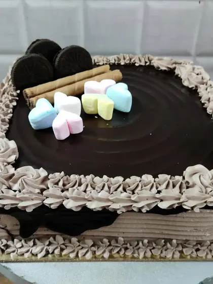 A square chocolate cake topped with Oreos, wafer rolls, and colorful heart-shaped marshmallows.