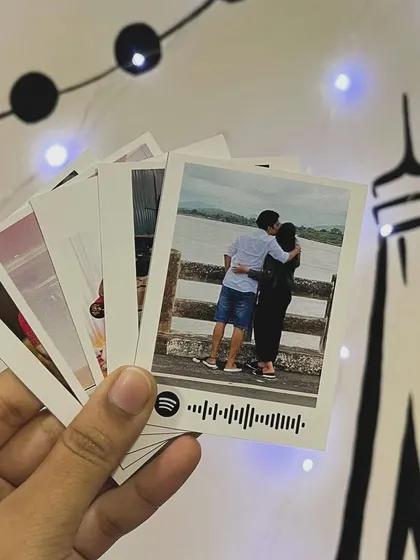 A hand holding a fan of polaroid prints, each with a unique photo and some with Spotify codes.
