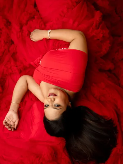 A playful top-down shot on a bed of vibrant red fabric. The joyful expression and bold color make this a standout portrait.