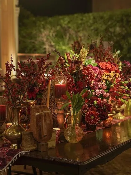 A long wooden table set for dinner, adorned with a runner of rich, colorful florals and candles. The design creates a warm and inviting atmosphere for a communal feast.