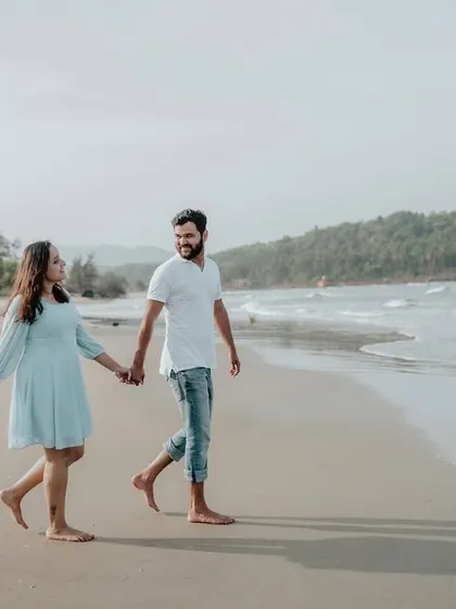 A full-length shot of the couple walking hand-in-hand, showcasing the beautiful expanse of the beach and sea.