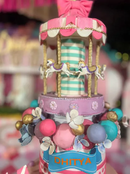 The carousel topper on this carnival cake is a masterpiece in itself, with tiny horses and intricate gold detailing.