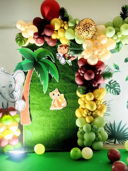 A fun corner at Dhyaan's jungle party, featuring an elephant cutout and a palm tree against a green hedge and leaf-print backdrop.