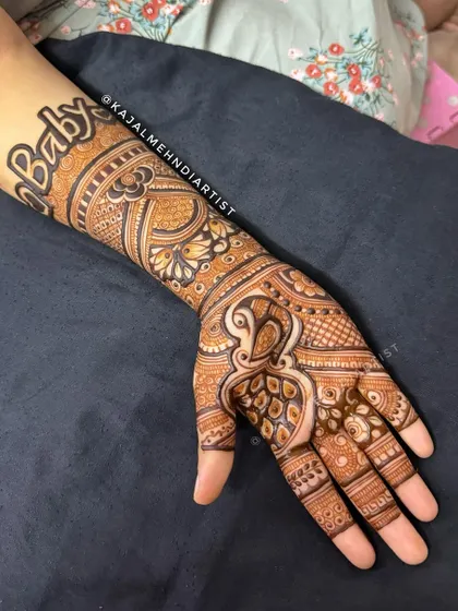 A modern and stylish baby shower design. The word "Baby" is written in a bold, artistic font on the forearm, paired with a detailed peacock and paisley pattern on the hand.