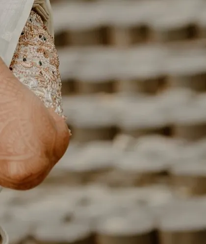 An artistic close-up focusing on the intricate details of a bride's embroidered blouse sleeve and the mehndi on her arm.