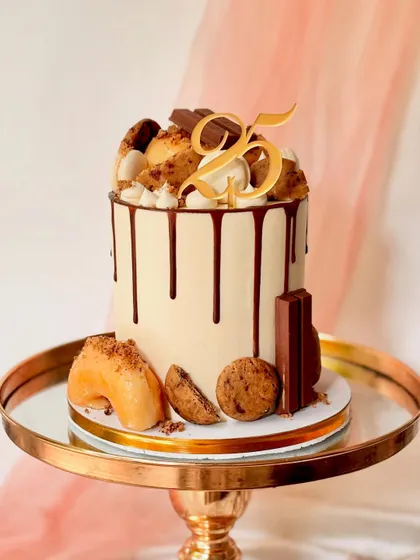My signature modern drip cake, perfect for a milestone 25th birthday. This tall cake has a smooth buttercream finish, a rich chocolate drip, and is generously topped with donuts, cookies, and chocolate bars.