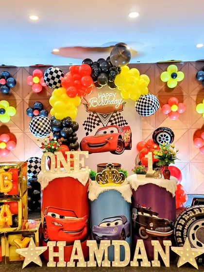 The full setup for a Cars first birthday, featuring themed pedestals, 'BABY' blocks, and a balloon wall.