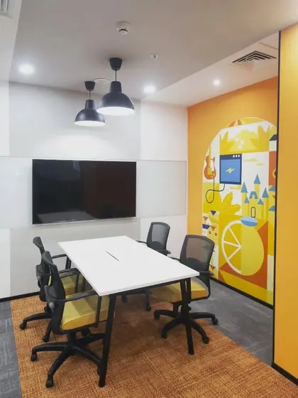 A small, functional meeting room designed for focused collaboration. The space includes a large screen for presentations, a whiteboard wall for ideation, and a colorful mural to keep the creative energy flowing.