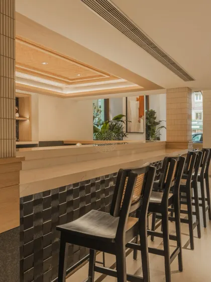 The main bar is crafted from light wood and features a textured black tile front, providing a subtle contrast while maintaining the minimalist aesthetic.