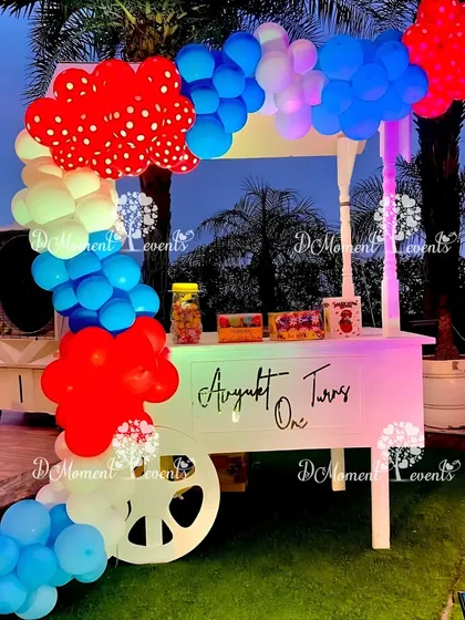An adorable candy and popcorn cart for a carnival party, decorated with a colorful balloon arch, perfect for serving treats at an outdoor event.