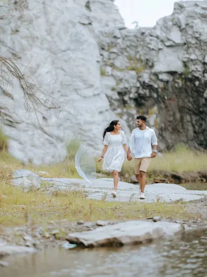 A couple walks hand-in-hand along the edge of a quarry lake. The wide shot emphasizes the beautiful, rugged landscape surrounding them.
