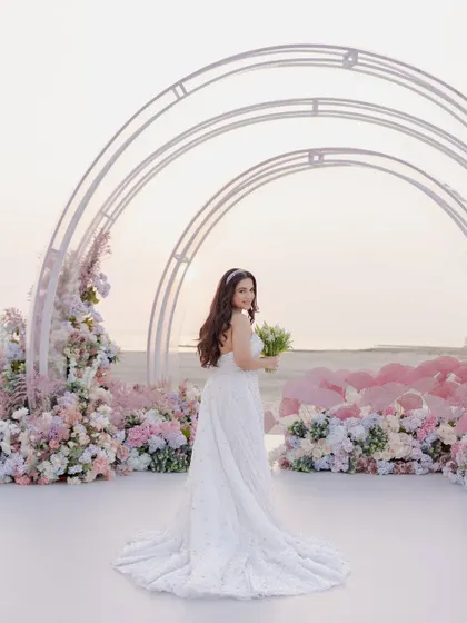 The bride at her dreamy beachside engagement in Bahrain. The pastel floral decor and modern arches perfectly complement the serene ocean backdrop.