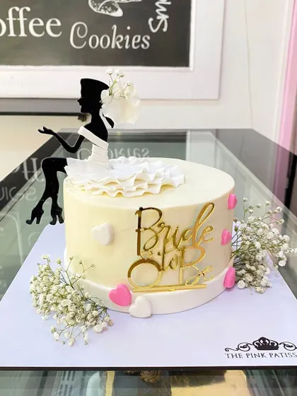 A perfect cake for a bridal shower, this design features a "Bride to Be" topper and a stylish silhouette of a bride. The simple white cake is accented with baby's breath and small pink hearts.