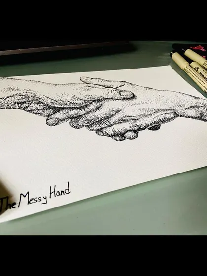 The original stippling artwork of the holding hands on my desk, next to the Micron pens I used to create it. This shows the piece in its raw, unfiltered form.