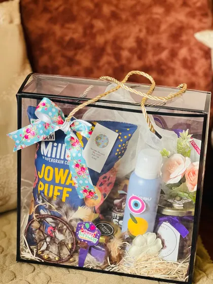 A premium gift hamper in a transparent bag, perfect for birthdays or anniversaries. It's filled with snacks, a drink, a candle, and other decorative items.