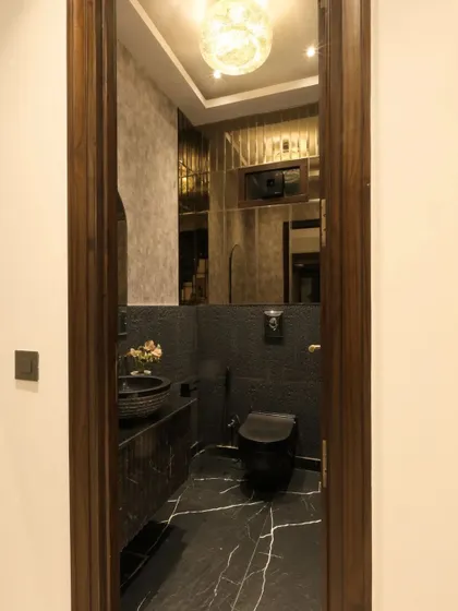 This monochrome powder room creates a dramatic atmosphere with textured black walls, bronze mirror paneling, and a statement chandelier.