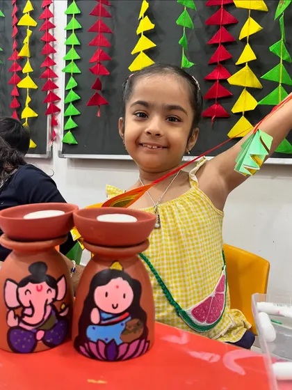 A smiling student with her hand-painted tea-light holders from our Diwali workshop.