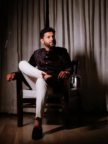 A moody portrait of the groom seated against a curtained backdrop.