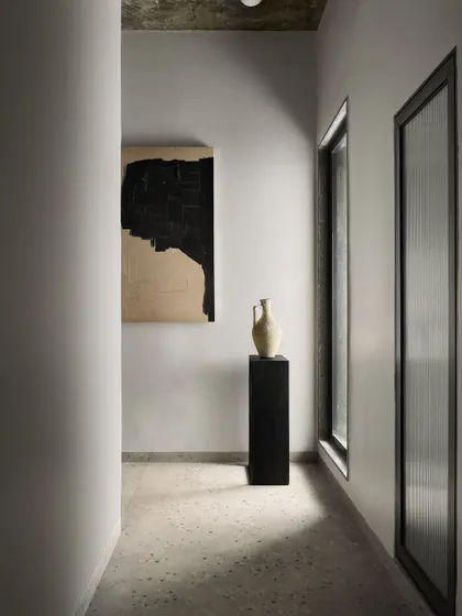 A minimalist corridor in Pavilion House, where a piece of abstract art and a simple pedestal create a gallery-like feel.