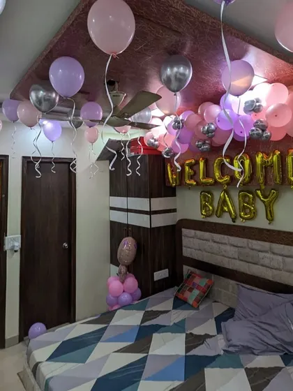 This angle shows the arrangement of pink, purple, and silver balloons floating on the ceiling of a bedroom for a baby welcome event.