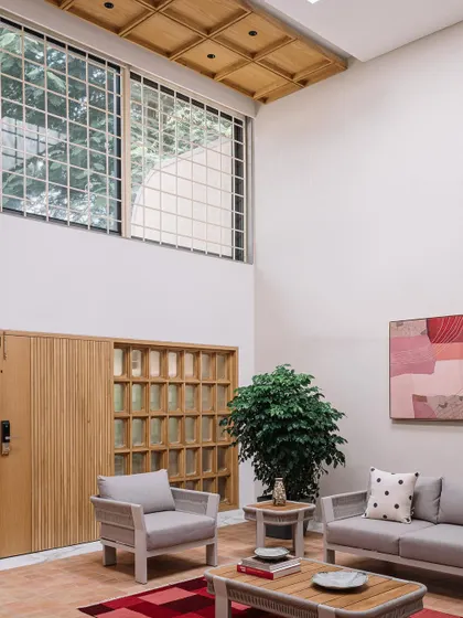 **Cocoon House, Ahmedabad:** We used large windows and glass blocks to ensure the living space is filled with diffused natural light. The coffered wooden ceiling and slatted wooden door add texture and warmth, balancing the minimalist feel with tactile details.