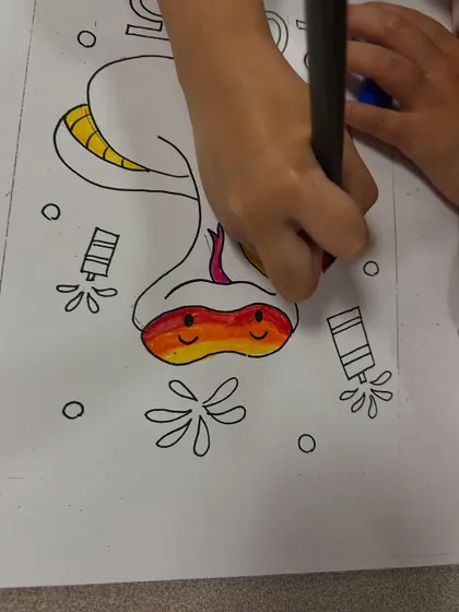 A student carefully colours their snake craft, choosing a beautiful sunset gradient for its face.