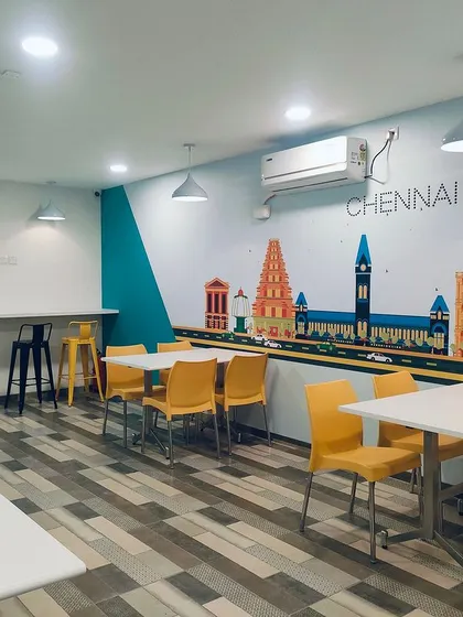The canteen at the TVS Auction Centre features a large mural of Chennai's skyline. We used bright yellow chairs and simple white tables to create a cheerful and functional dining space that celebrates local identity.