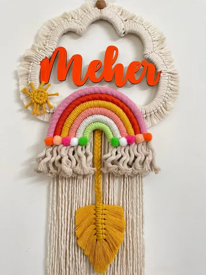 A warm-toned rainbow dreamcatcher for 'Meher'. This piece features a macrame leaf and a bright sun, adding a lovely bohemian touch to her room.